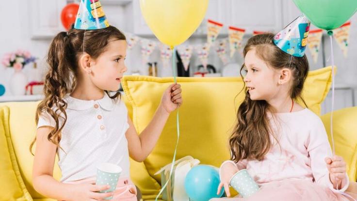 zwei mädchen tragen geburtstagsmützen und halten geburtstagsballons